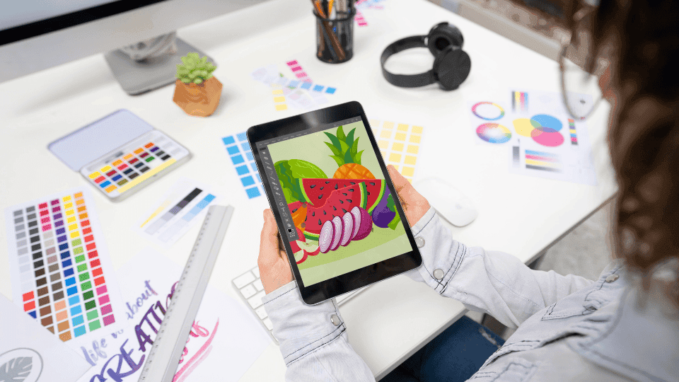 Designer reviewing vibrant fruit art on a tablet, showcasing creativity in Logo Design.